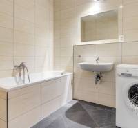 Koupelna s vanou, umyvadlem a pračkou v 3-pokojovém bytě. Stěny s béžovým obkladem.