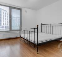 Ložnice v třípokojovém bytě s kovovou postelí a podlahou s dřevěným dekorem.