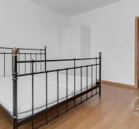 Ložnice třípokojového bytu s kovovou postelí a podlahou s dřevěným dekorem.