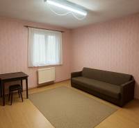 Pokoj v rodinném domě s hnědou pohovkou, stolem a podlahou s dřevěným dekorem.