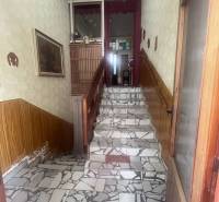 Schodiště s mozaikovou dlažbou, dřevěným zábradlím a ozdobnou tapetou v rodinném domě.