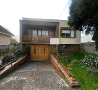 Rodinný dům v Šaľe s garáží, balkonem a zahradou, obklopený vegetací a plotem.