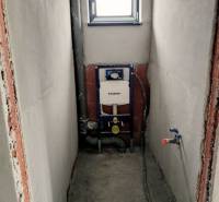 Stavební příprava pro WC v rodinném domě se zabudovanou nádržkou, bílými stěnami a malým oknem.