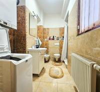 Koupelna s pračkou, umyvadlem, toaletou a světlou keramickou dlažbou ve 3-pokojovém bytě.