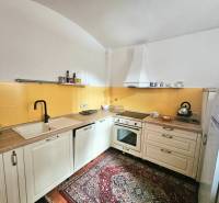 Kuchyně v 3-pokojovém bytě s krémovými skříňkami, žlutým obkladem a vzorovaným kobercem.