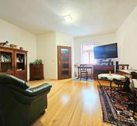 Obývací pokoj v 3-pokojovém bytě s podlahou s dřevěným dekorem, vybavený sedačkou a televizorem.