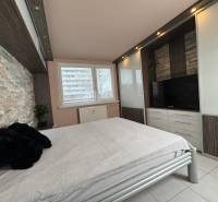 Ložnice v 3-pokojovém bytě s kamenným obkladem a vestavěnou skříní s televizorem.