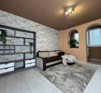 Obývací pokoj v 3-pokojovém bytě s pohovkou, policemi a dekorativní stěnou.