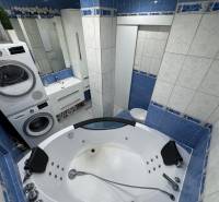 Koupelna v 3-pokojovém bytě s rohovou vanou, pračkou, sušičkou a umyvadlem.