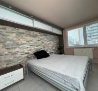 Ložnice s kamennou stěnou a velkým oknem v 3-pokojovém bytě.