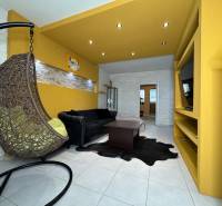 Obývací pokoj v 3pokojovém bytě s houpacím křeslem, černou pohovkou a žlutými stěnami.
