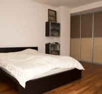 Ložnice v rodinném domě s postelí a skříní, podlaha s dřevěným dekorem.