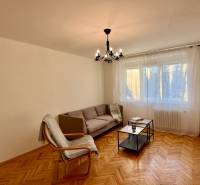 Obývací pokoj s pohovkou, křeslem, lustrem a podlahou s dřevěným dekorem ve 3-pokojovém bytě.