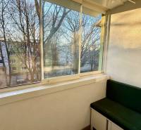 Zasklený balkon ve 3-pokojovém bytě se zelenou lavicí a výhledem na stromy.