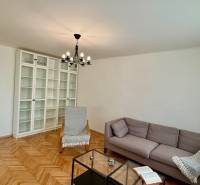 Obývací pokoj v 3-pokojovém bytě s podlahou s dřevěným dekorem, světlým nábytkem a pohovkou.