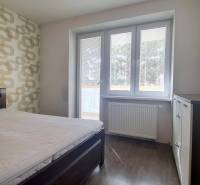 Ložnice v 2pokojovém bytě s postelí, vzorovanou tapetou a podlahou s dřevěným dekorem.