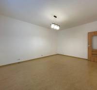 Prostorný pokoj v 2pokojovém bytě s podlahou s dřevěným dekorem a bílými stěnami.