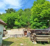 Rodinný dům v Hajnáčce s dřevem a zelení na dvoře, obklopený bujnou přírodou.