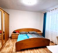 Ložnice v rodinném domě s postelí, skříní a podlahou s dřevěným dekorem.