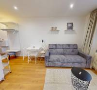 Garsonka s pohodlnou sedačkou, stolkem a podlahou s dřevěným dekorem.