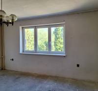 Pokoj v rodinném domě s velkým oknem, původním lustrem a výhledem na zeleň.