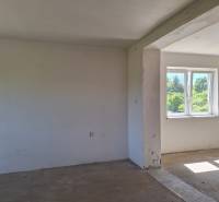 Nezařízená místnost v rodinném domě s výhledem do zahrady přes plastové okno.