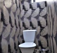 Toaleta s dekorativní tapetou s listovým vzorem a malým oknem výše.