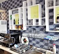 Interiér obchodních prostor s kávovarem, regály, sklenicemi a nápoji na poličkách.