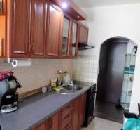 Kuchyně ve 3-pokojovém bytě s dřevěnými skříňkami a kachličkovou stěnou nad pracovní deskou.