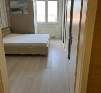 Ložnice se světlým nábytkem, velkým oknem a podlahou s dřevěným dekorem ve 4pokojovém bytě.