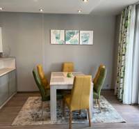 Jídelní kout ve 4-pokojovém bytě s pestrými židlemi a podlahou s dřevěným dekorem.