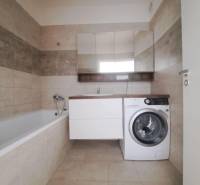 Koupelna v 2-pokojovém bytě s vanou, pračkou a béžovými obklady.