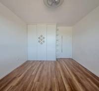 Pokoj s podlahou s dřevěným dekorem, vestavěnou skříní a poličkami v 2pokojovém bytě.