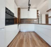 Kuchyně v 2-pokojovém bytě s bílými skříňkami a podlahou s dřevěným dekorem.