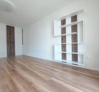 Obývací pokoj v 2pokojovém bytě s podlahou s dřevěným dekorem a bílými stěnami.