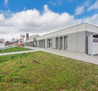 Na ulici Vajanského jsou obchodní prostory, vedle chodníku je zelený trávník.