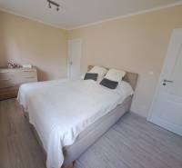 Ložnice v rodinném domě s postelí, komodou a podlahou s dřevěným dekorem.