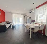 Obývací pokoj v rodinném domě s červenou stěnou, šedou dlažbou a bílým nábytkem.