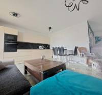 Obývací pokoj v rodinném domě s otevřenou kuchyní a jídelním stolem. Podlaha s dřevěným dekorem.