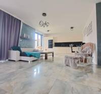 Obývací pokoj s velkými okny a světlými dlaždicemi v rodinném domě.