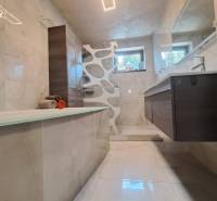 Koupelna v rodinném domě s vanou, moderním osvětlením, dlažbou a umyvadlem.