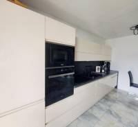 Kuchyně v rodinném domě s lesklou linkou a vestavěnými spotřebiči, podlaha s mramorovým vzorem.