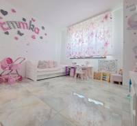 Dětský pokoj v rodinném domě s dekoracemi, kočárkem a psacími stoly. Podlaha má dřevěný dekor.