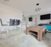 Interiér rodinného domu se světlými dlaždicemi, moderním nábytkem a stěnou s televizorem.