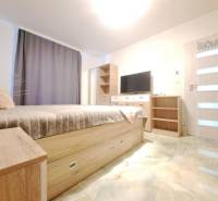 Ložnice v rodinném domě s postelí, šatní skříní, televizorem a podlahou s dřevěným dekorem.