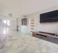 Obývací pokoj v rodinném domě s televizí na stěně, stanem a keramickou podlahou.