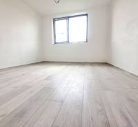 Pokoj rodinného domu s podlahou s dřevěným dekorem, bílé stěny, jedno okno.