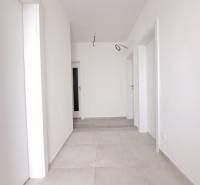 Světlá chodba v rodinném domě s bílými stěnami a světlou dlažbou.