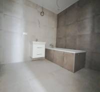 Koupelna v rodinném domě s obkladem a vanou na neutrální dlažbě.