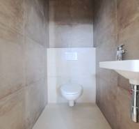 Toaleta v rodinném domě s béžovým keramickým obkladem a umyvadlem.